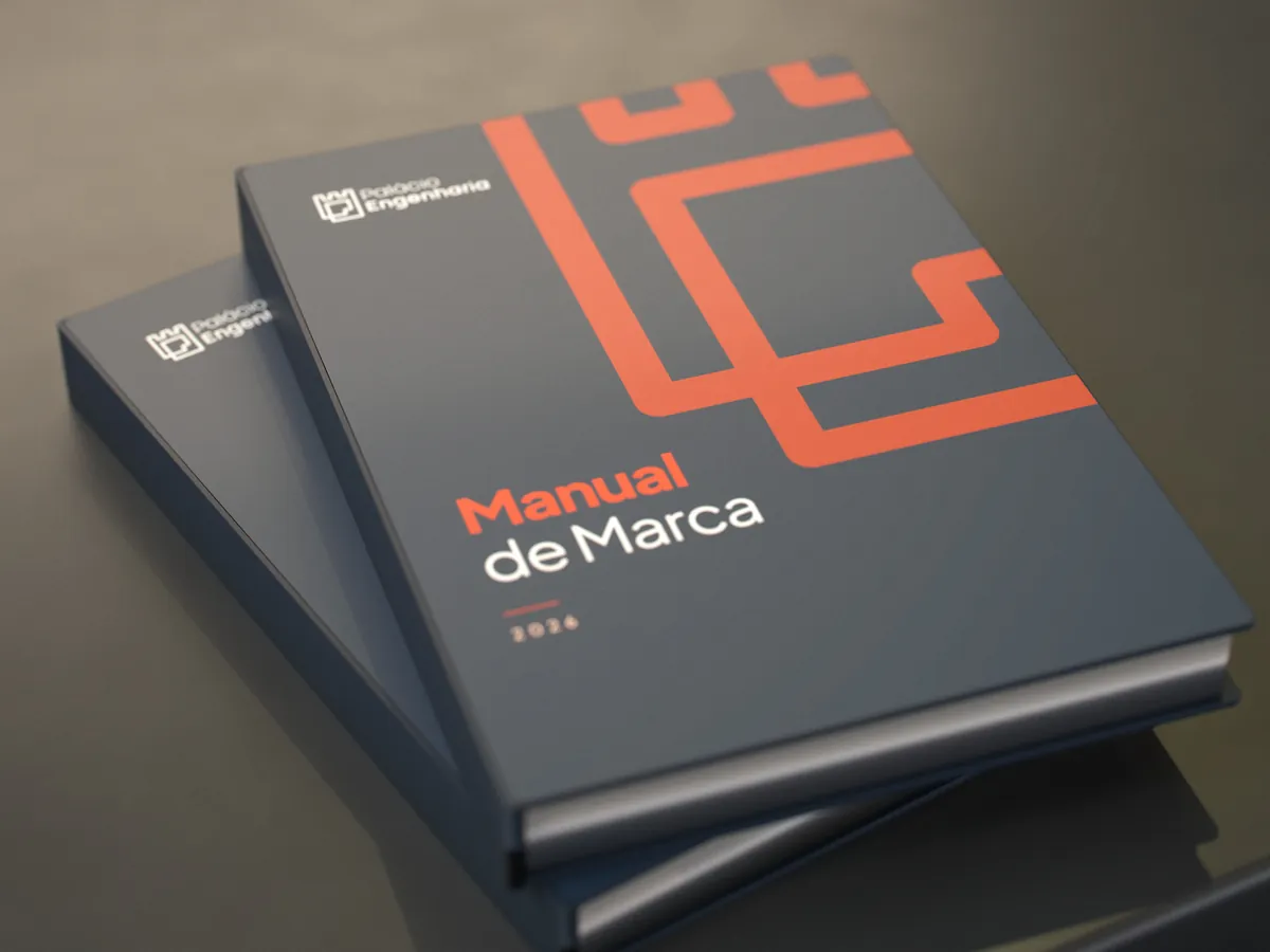 Os dois manuais em capa dura, um sobre o outro, sobre a mesa de pedra: Manual de Marca em cima, Manual de Comunicação embaixo, com o ícone laranja ampliado na capa azul-marinho